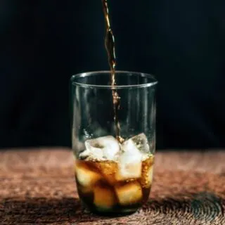 Coffee being poured into a glass with ice cubes.