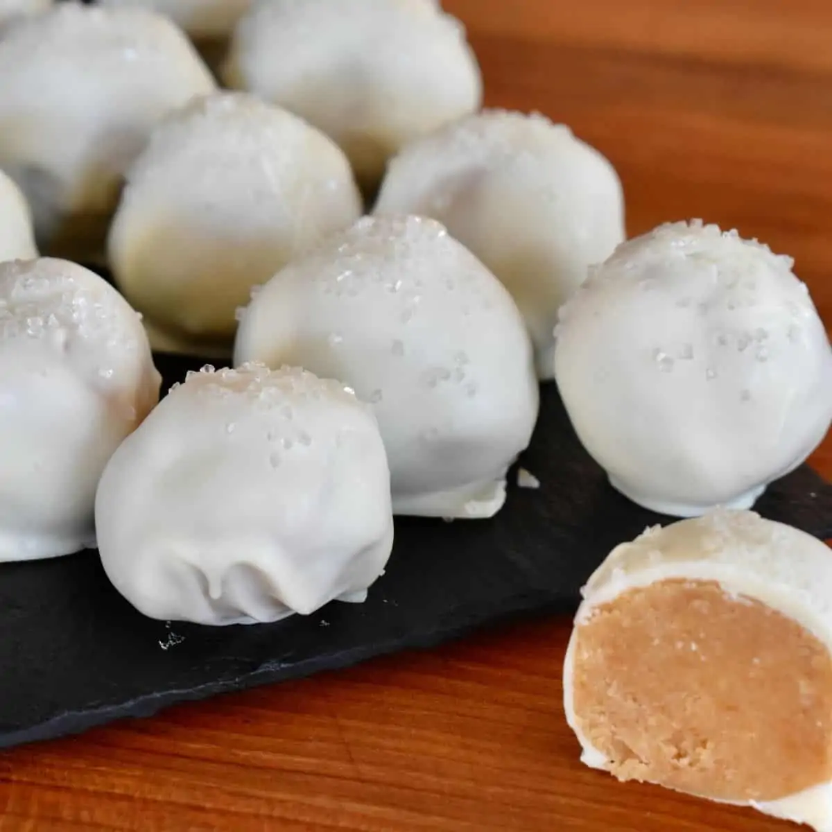 No-bake white chocolate oreo truffle balls on black plate with one piece on the side cut in half to showcase what's inside.
