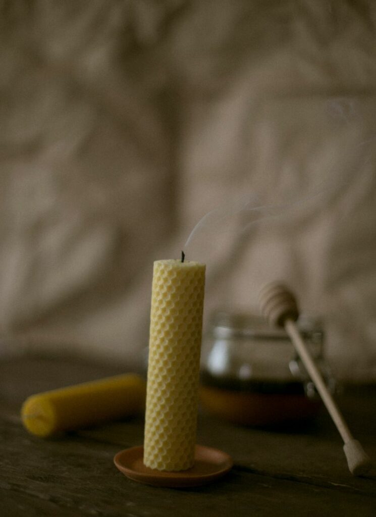 Rolled beeswax candle with smoke but no flame. Honey dipper on the background.