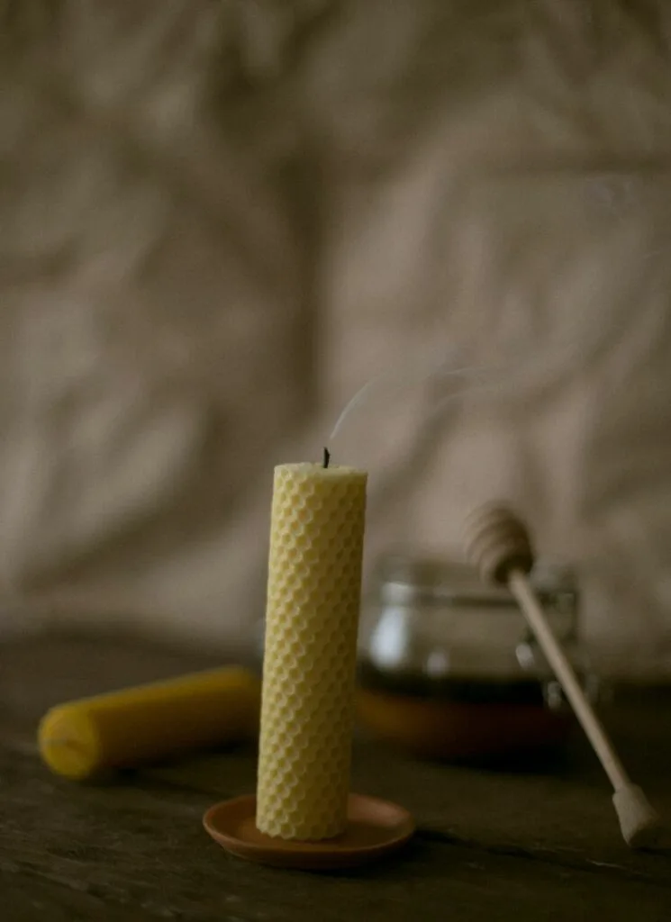Rolled beeswax candle with smoke but no flame. Honey dipper on the background.