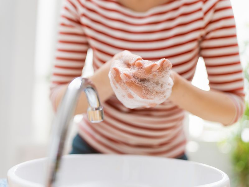 A woman wearing stripe red and white shirt washing her hands with soap in front of the sink.