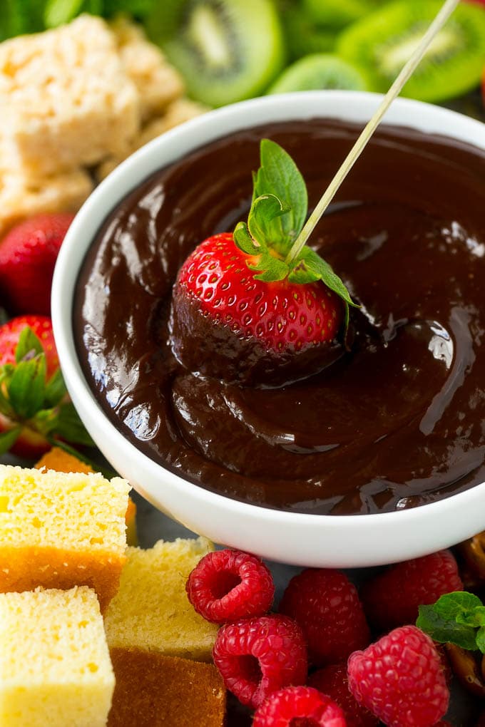 Chocolate fondue in the middle of the fruit platter with a piece of strawberry being dipped in it.