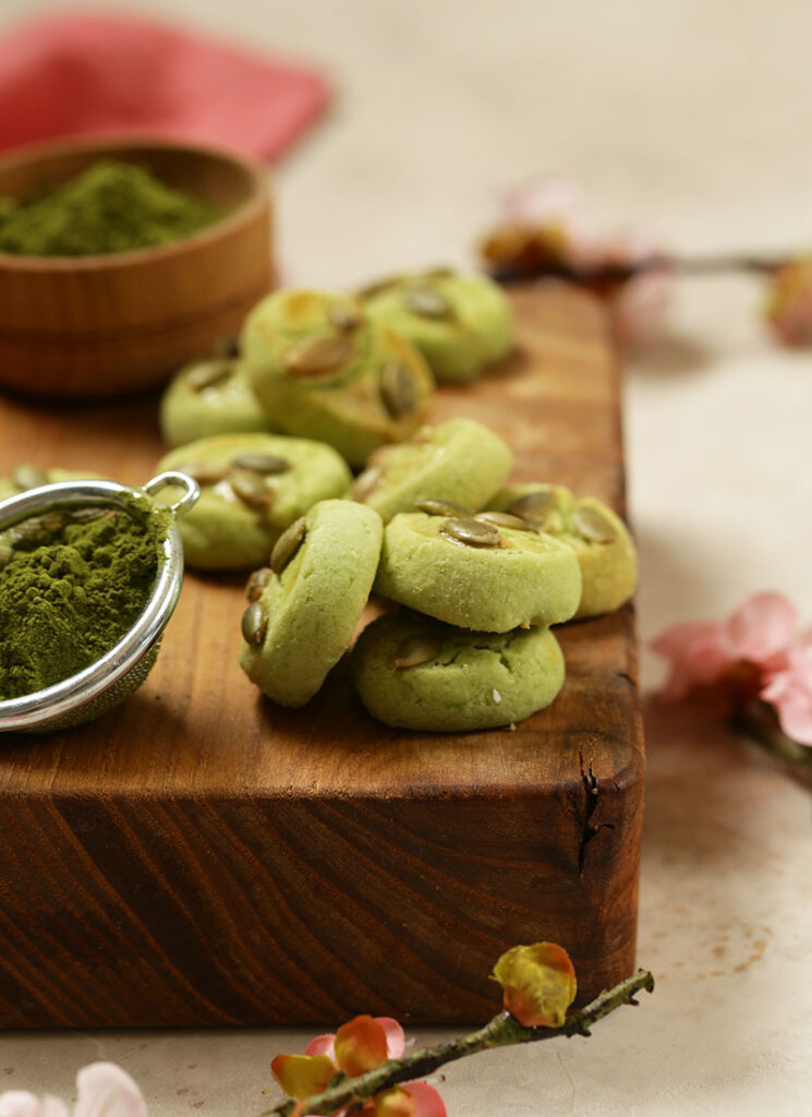 Matcha sugar cookies next to a scoop of match powder on wooden chopping board.