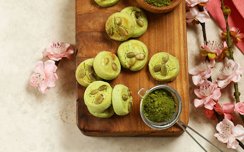 Matcha sugar cookies next to a scoop of match powder on wooden chopping board.