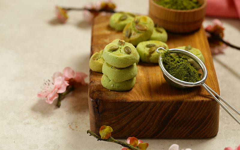 Side view of matcha sugar cookies next to a scoop of match powder on wooden chopping board.