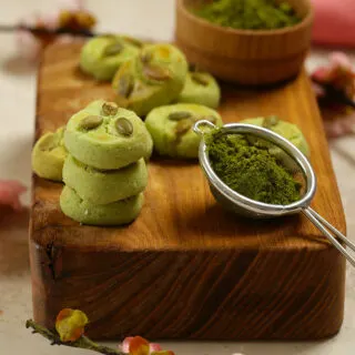 Close up photo of matcha sugar cookies next to a scoop of match powder on wooden chopping board.