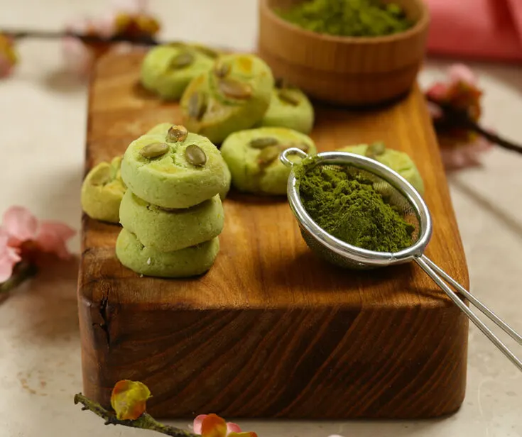 Close up photo of matcha sugar cookies next to a scoop of match powder on wooden chopping board.