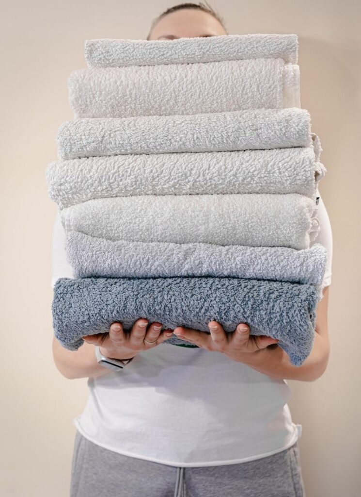 A person holding a stack of clean cotton towels.