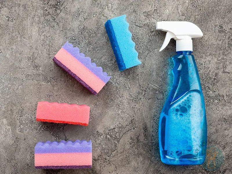 A blue spray bottle next to four colorful sponges.