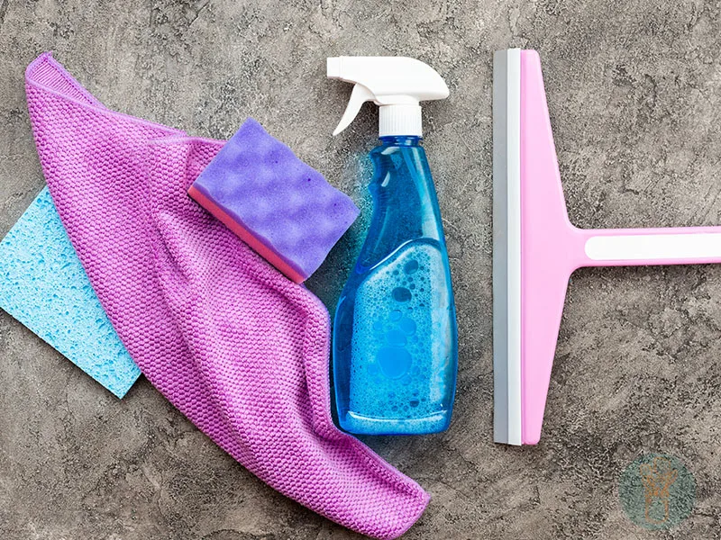 DIY all-purpose cleaner in blue spray bottle next to a washcloth and other cleaning materials.