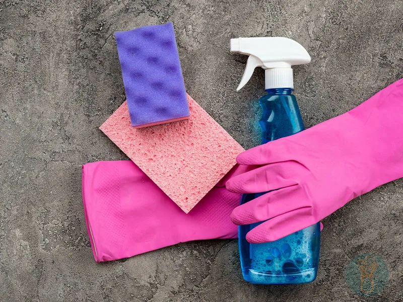 DIY all purpose cleaner in blue spray bottle next to sponges and a pair of pink rubber gloves.
