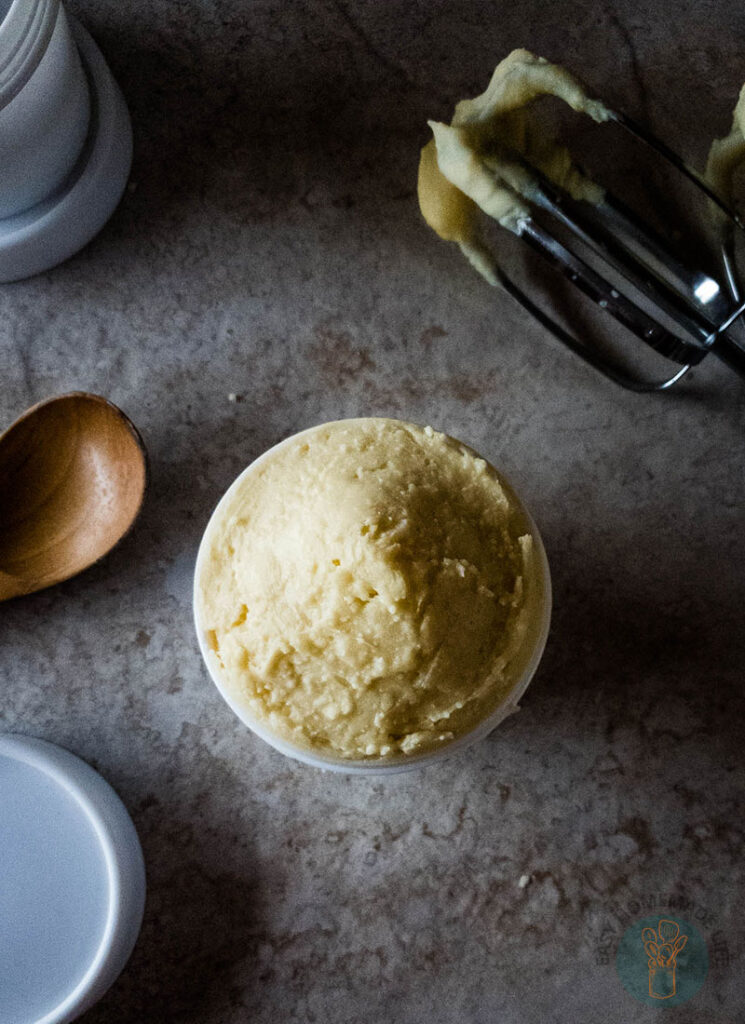 Beard butter in white container next to a wooden spoon.