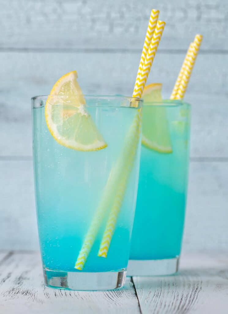 Two glasses of electric blue lemonade drink with yellow straws and lemon wedges.