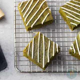 Four square slices of matcha brownies with white chocolate icing in a cooling rack.