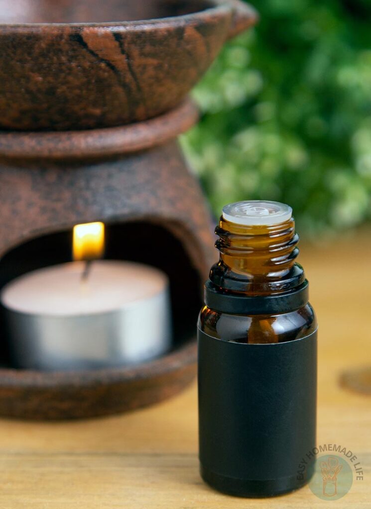A bottle of woodsy essential oil blend next to an oil burner diffuser.