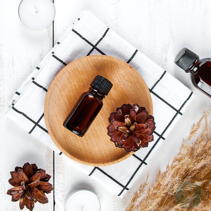 A wooden plate with pine cones and a bottle of woodsy essential oil blend.