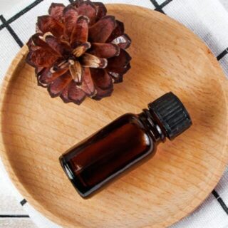 A wooden plate with a bottle of essential oil and a pine cone.