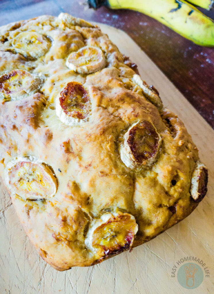 A whole banana bread on a wooden board with banana background.