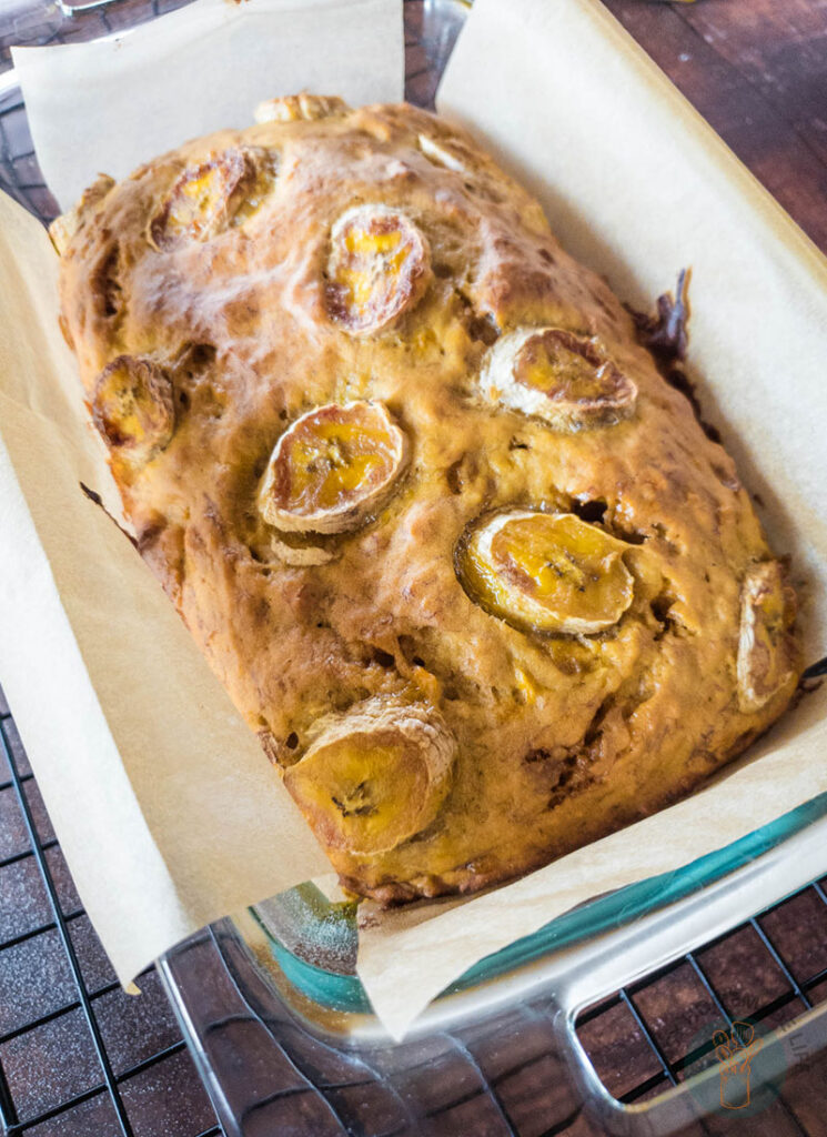 A whole banana bread in a baking dish placed on a cooling rack.