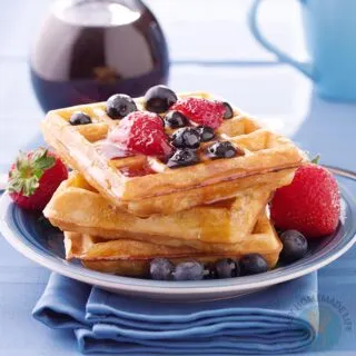 Dairy-free waffles in a stack garnished with berries next to a bottle of syrup.