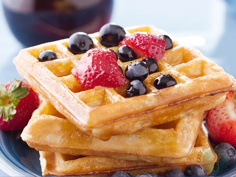 Three dairy-free waffles in a stack garnished with strawberries, blueberries and syrup.