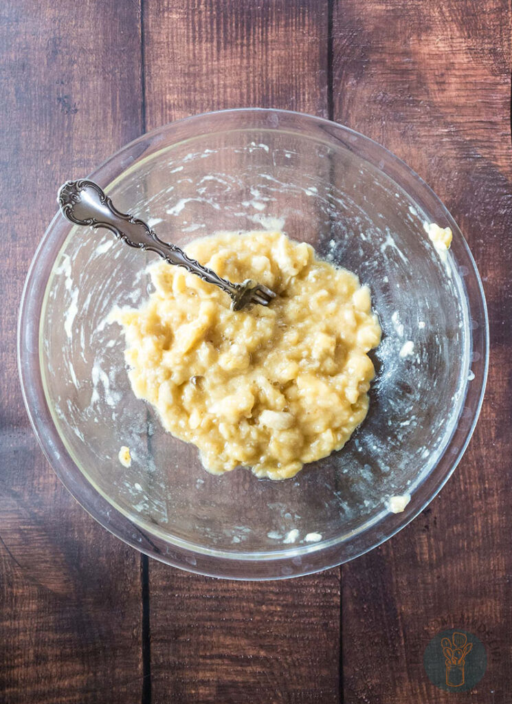 Mashed bananas in a glass bowl with a fork.