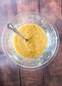 Mashed bananas with egg and sugar in a glass bowl with a fork.