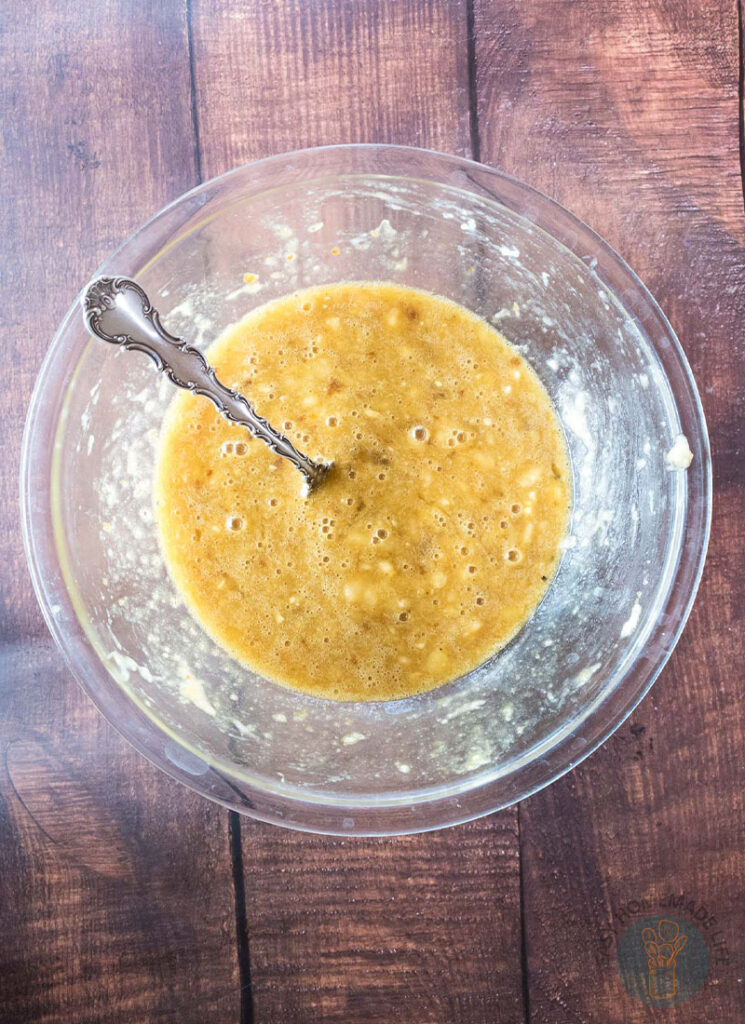 Mashed bananas with egg and sugar in a glass bowl with a fork.