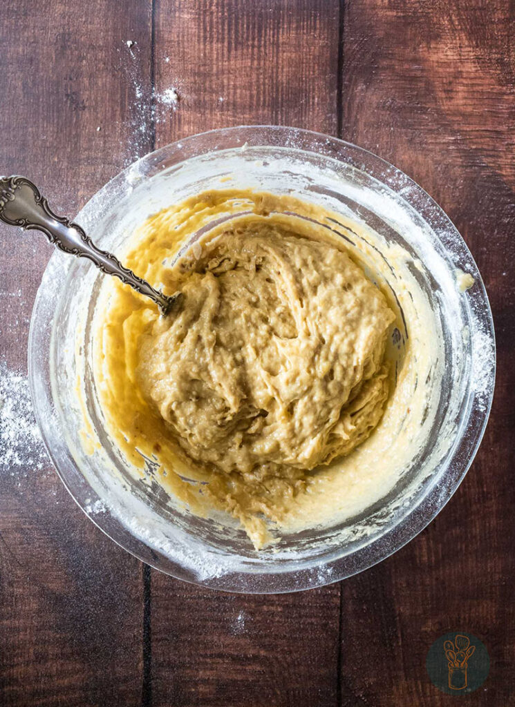 Mashed bananas mixture with flour added in a glass bowl with a fork.