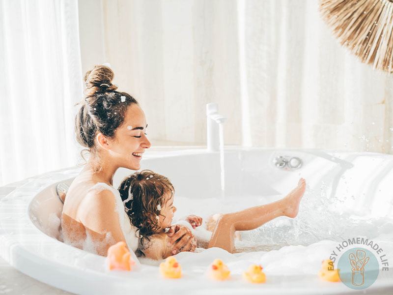 A woman and a little girl enjoying a bubble bath with rubber duckies on the side of the bath tub.