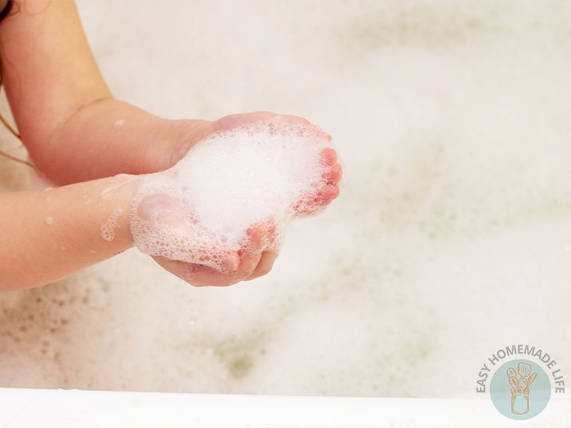 A child holding bubbles from the bubble bath with two hands.