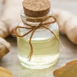 A bottle of ginger oil next to some ginger.