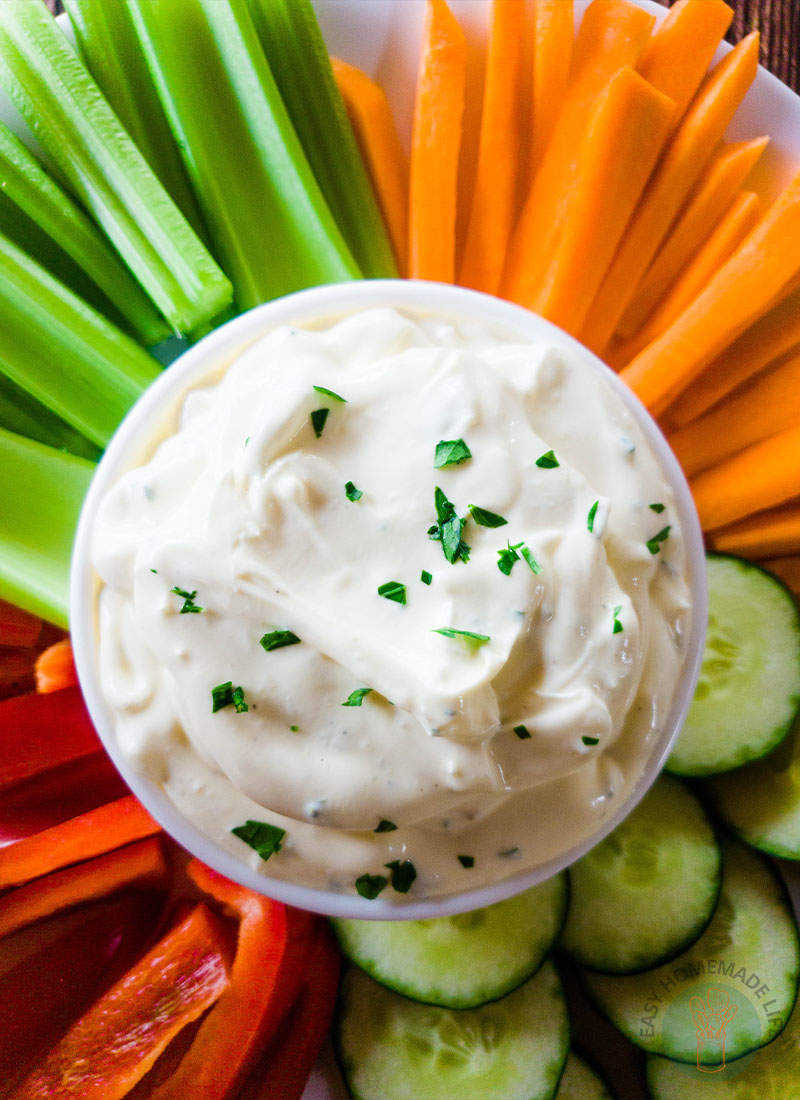 3-ingredient easy onion dip in the middle of a plate full of celery sticks, carrots and red bell pepper cut in stripes and cucumbers cut in circle.