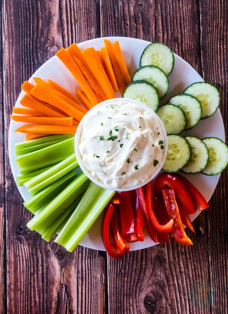 3-ingredient easy onion dip in the middle of a plate full of celery sticks, carrots and red bell pepper cut in stripes and cucumbers cut in circle.