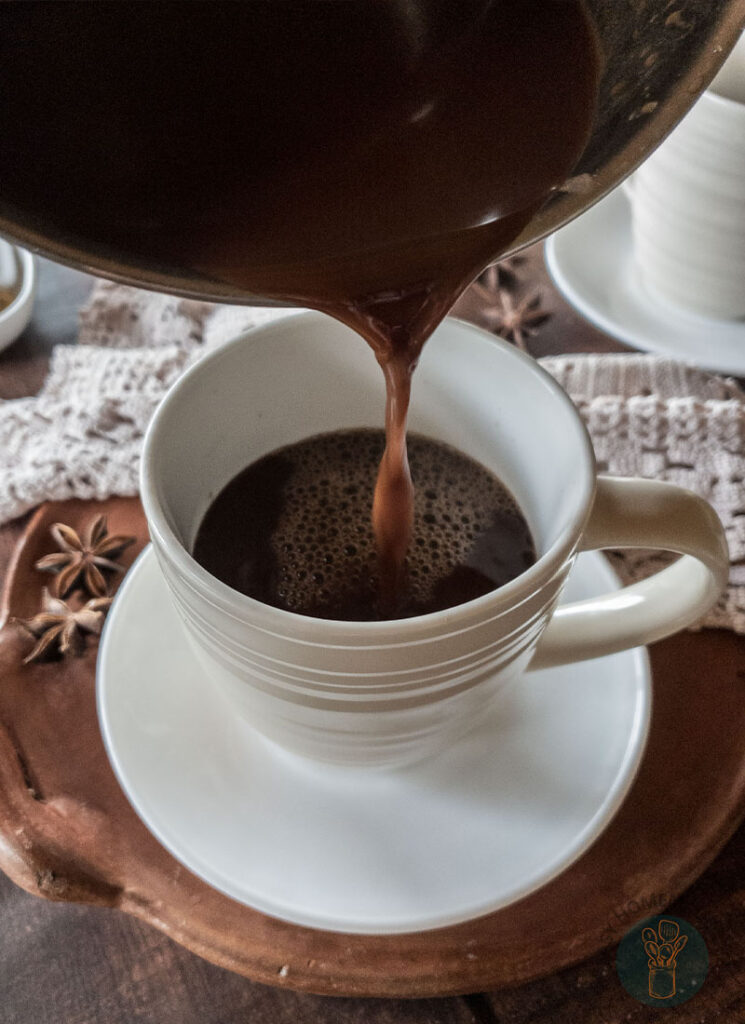 Hot chocolate chai tea being poured on a white teacup.