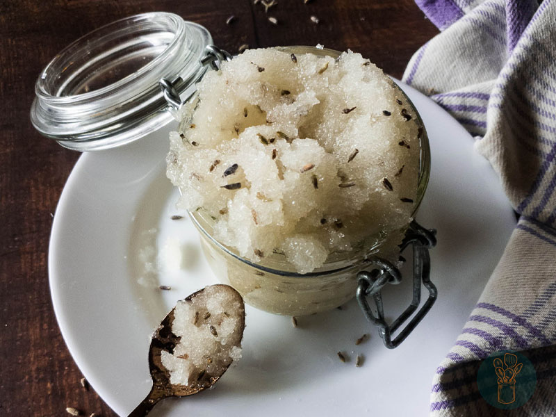 A jar of lavender scrub next to a spoon in a white plate.