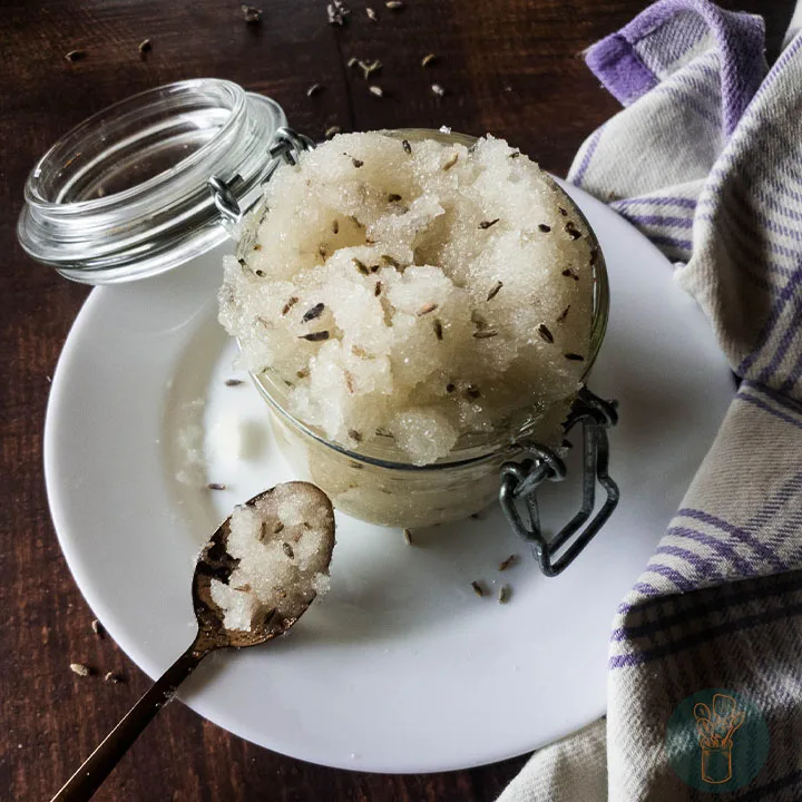 A jar of lavender scrub on a plate placed on top of a wooden table.