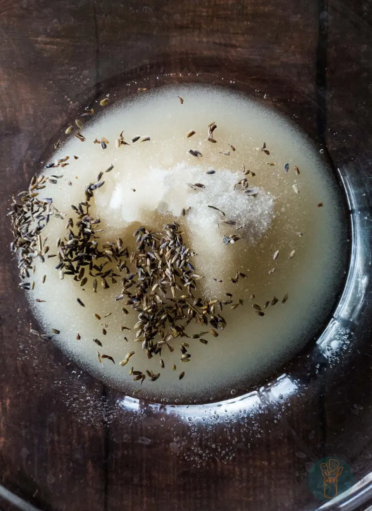 A mixture of lavender sugar scrub in a clear glass bowl.