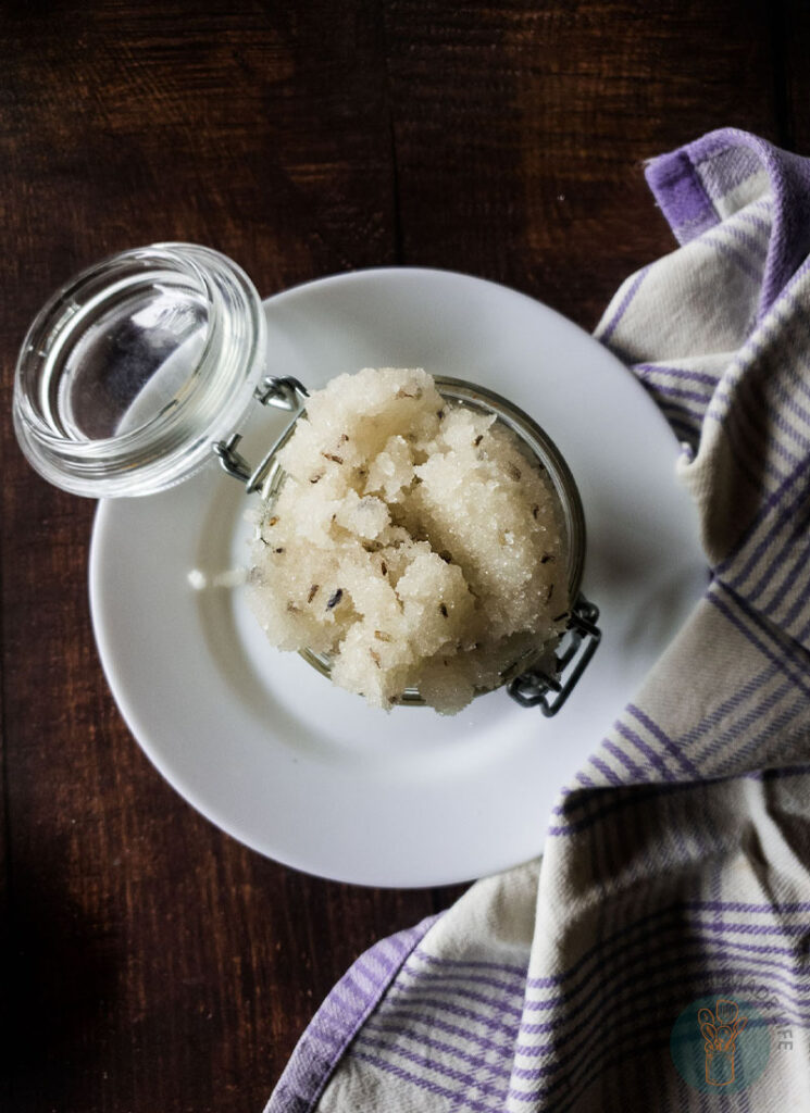 A jar of lavender sugar scrub on a white plate next to a purple and white napkin.