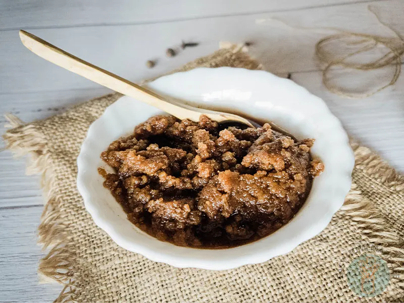 Pumpkin pie spice facial scrub in a white bowl with a wooden spoon placed on a wooden table with burlap design.