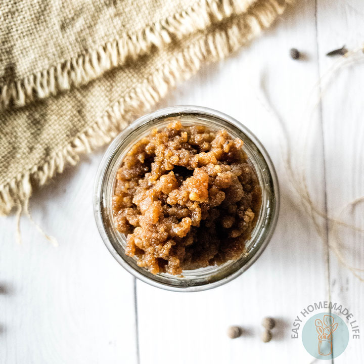 A jar of brown sugar facial scrub next to a burlap on a white wooden surface.