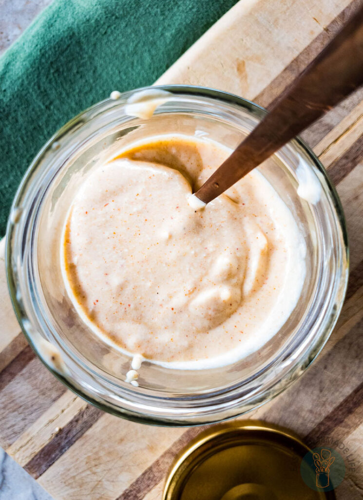 A jar of tiger sauce with a spoon on a wooden cutting board.