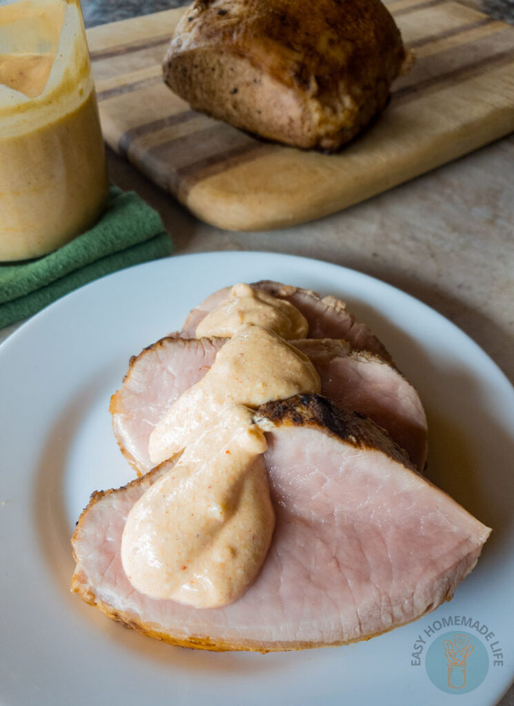 Tiger sauce over slices of cooked meat on a white plate next to a jar of the same sauce and a slab on meat on a wooden cutting board.