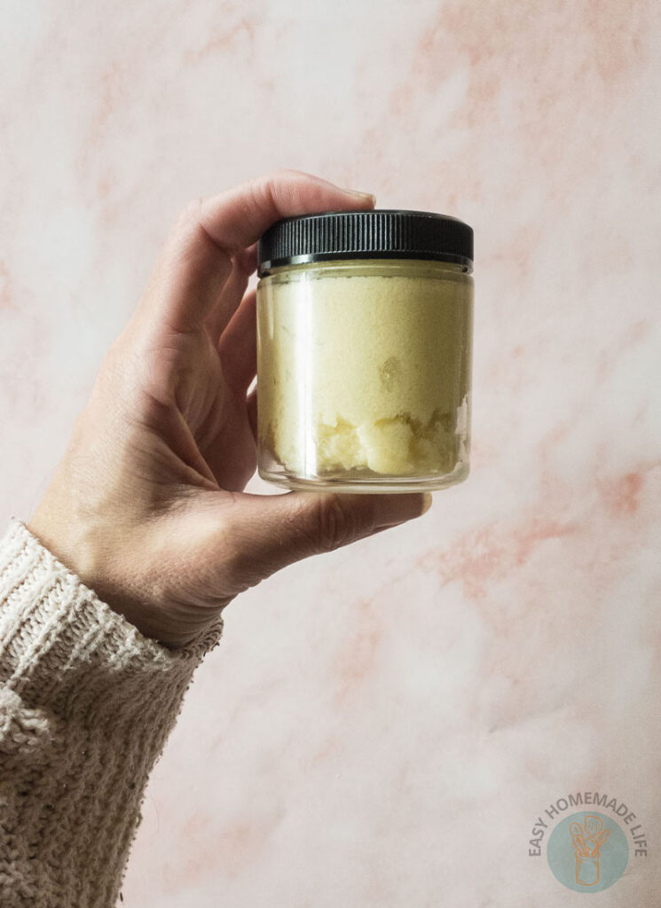 A person holding a jar of shea butter body scrub.