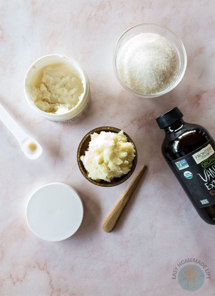 Whipped sugar scrub in wooden bowl next to bowls of its ingredients.