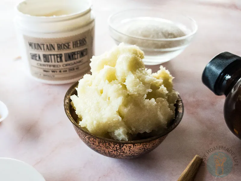 Whipped sugar scrub in wooden bowl next to a bowl of sugar and a bottle of vanilla extract.