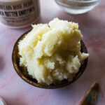 Whipped sugar scrub in wooden bowl next to a jar of shea butter.