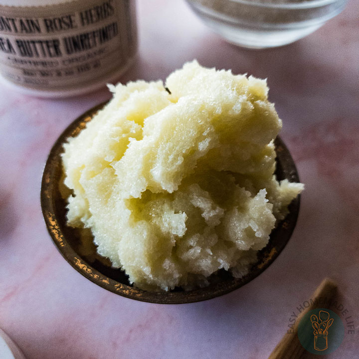 Whipped sugar scrub in wooden bowl next to a jar of shea butter.