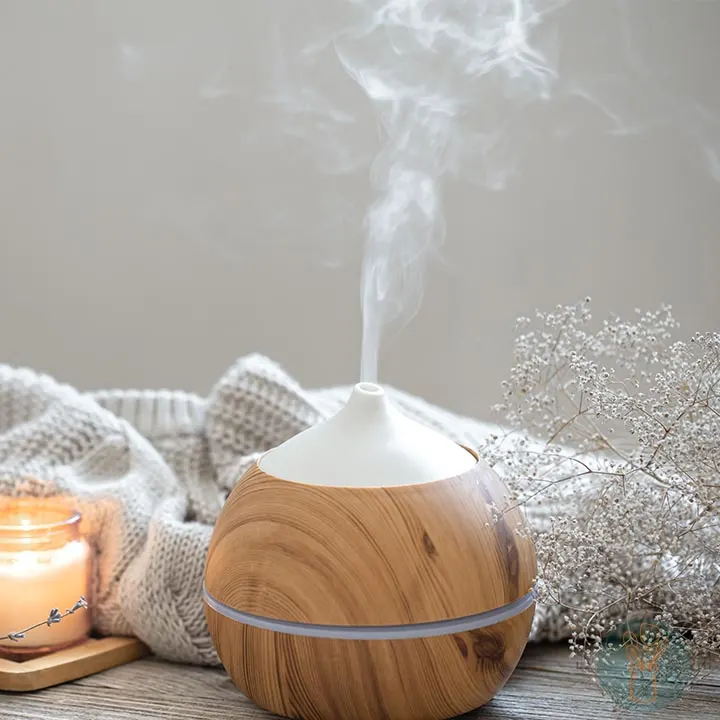 Essential oil diffuser diffusing mist next to a small lit candle in a jar.