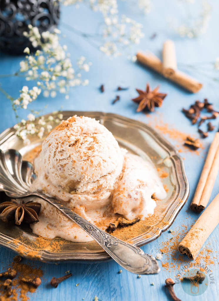 A scoop of chai ice cream garnished with cinnamon powder in a silver plate on a blue table.